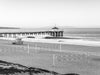 Sunrise over the Pacific Ocean at the Manhattan Beach Pier, with surfers and a small swell and decent surf, with volleyball courts and a lifeguard tower, in black and white