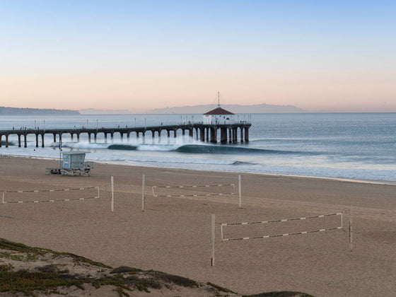 Sunrise over the Pacific Ocean at the Manhattan Beach Pier, with surfers and a small swell and decent surf, with volleyball courts and a lifeguard tower