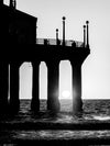 Manhattan Beach sunset shining through the pier's pilings about to reach the horizon in black and white. 