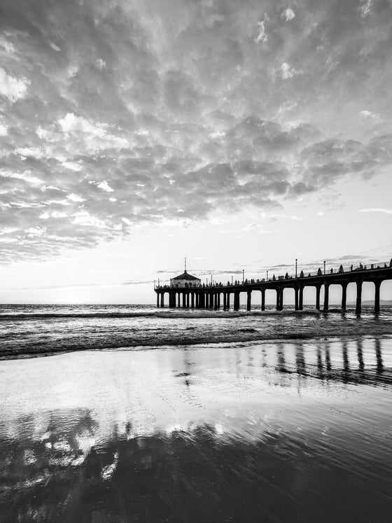 Manhattan Beach sunset with the cloudy sky reflecting across the sand and water in black and white.