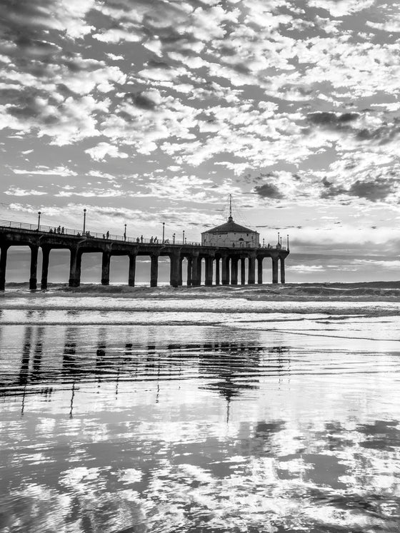 A sunset with popcorn-like clouds that reflect and create a beautiful contrast against the low tide ocean in black and white..