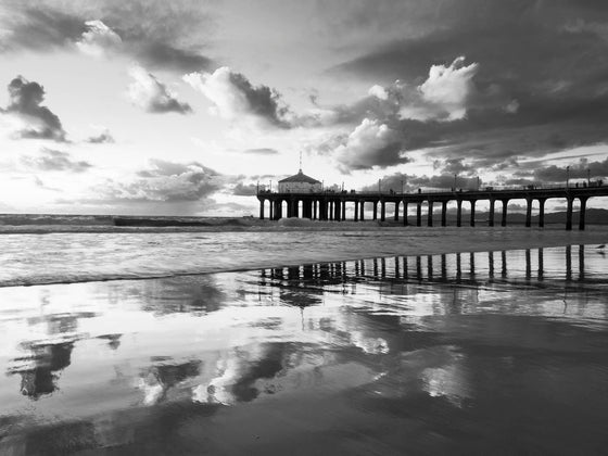 Manhattan Beach pier at sunset, during low tide, with the pier and clouds reflected in the sand, in black and white