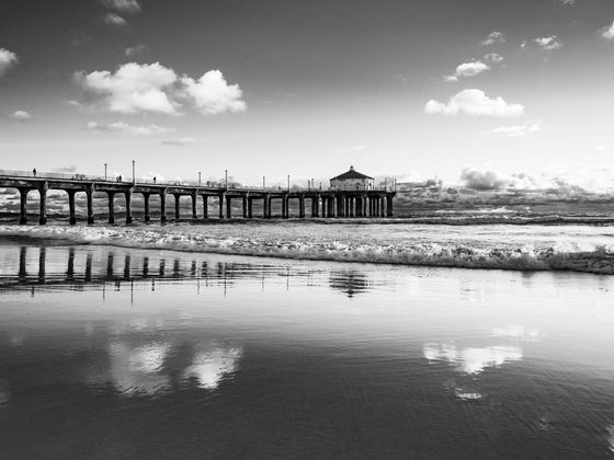Manhattan Beach California pier, at sunset, with clouds reflected on the sand in the beach, in black and white