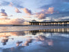 Manhattan Beach pier at sunset, during low tide, with the pier and clouds reflected in the sand, with blue, pink orange and yellow hues