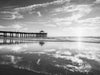 manhattan beach pier at sunset with a low tide and clouds reflecting in the sand, in black and white