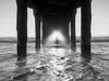under manhattan beach pier at sunset with sun streaming through the mist at sunset, in black and white