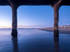Sunset photo of the Manhattan Beach Pier taken during sunset. Northern Manhattan Beach and the Santa Monica Bay can be seen in this photo. There are blue tones and the sand is reflecting the sky.