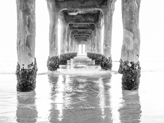 Photo of tunnel view from under the Manhattan Beach Pier. It is very minimalist, overcast  and the photo is muted in black and white.