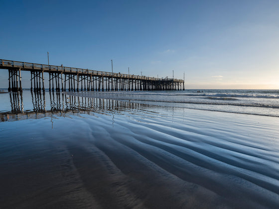 Newport Beach pier at low tide, with ripples of sand and a blue sky