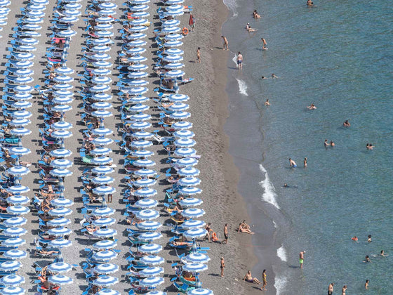 Blue and white beach umbrellas in rows on the Positano beach on the Amalfi coast in Italy in the summertime  to the left half with the ocean to the right half.