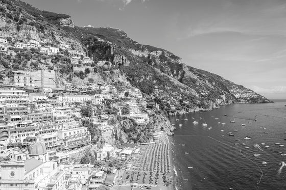 A horizontal photograph featuring the town of positano and the positano coastline in Italy, in black and white