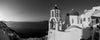A panoramic photograph that features the horizon of Oia in Sanotrini, specifically focusing on the white and blue church, in black and white