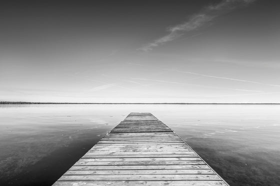 a dock on a calm, still lake in black and white