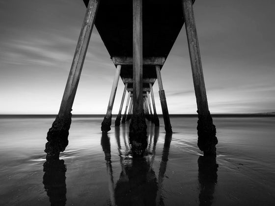 the Hermosa Beach pier at a super low tide, right after sunset, with a reflection of the clouds on the sand, in black and white