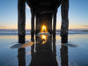 Under the Manhattan Beach Pier at low tide with the sun streaming in and mist and a starburst, during the annual pierhenge day when the setting sun lines up directly down the middle of the Manhattan Beach Pier