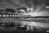 Sunset at the Hermosa Beach pier with dramatic orange and yellow clouds and sun rays breaking through them in black and white